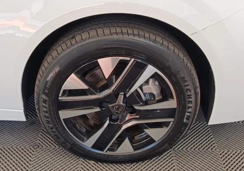 Gros plan sur la roue arrière droite d’une Peugeot 208 électrique blanche, jante alliage bicolore moderne.