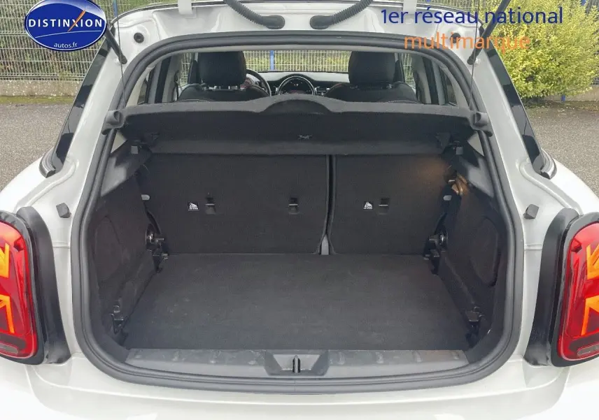 Coffre ouvert vu de l'arrière d'une MINI 1.5 136CH blanc nacré, montrant l'espace de chargement et la banquette arrière.