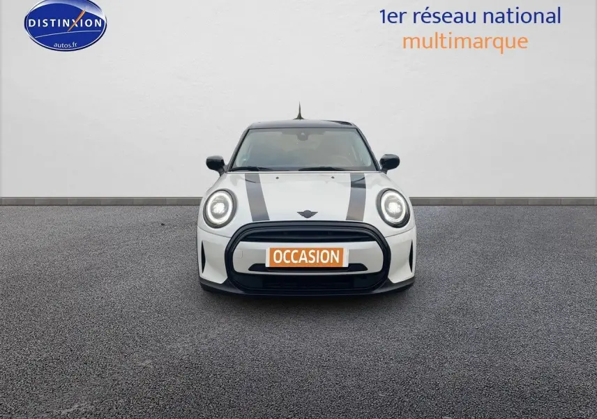 Vue frontale d'une MINI blanche nacrée 2023 avec bandes noires sur le capot et phares LED allumés.