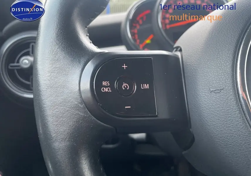 Gros plan sur le volant noir de la MINI 1.5 136CH STEPTRONIC 2023, avec commandes de régulateur de vitesse visibles.