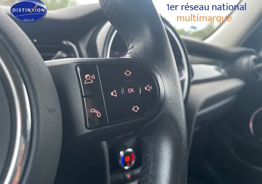 Gros plan sur les commandes du volant noir d'une MINI 1.5 136CH 2023, intérieur moderne avec tableau de bord en arrière-plan.