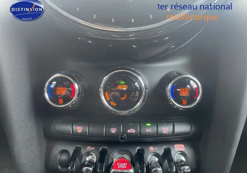 Gros plan sur la console centrale de la MINI blanche nacrée 2023, montrant les commandes de climatisation et le bouton start/stop rouge.