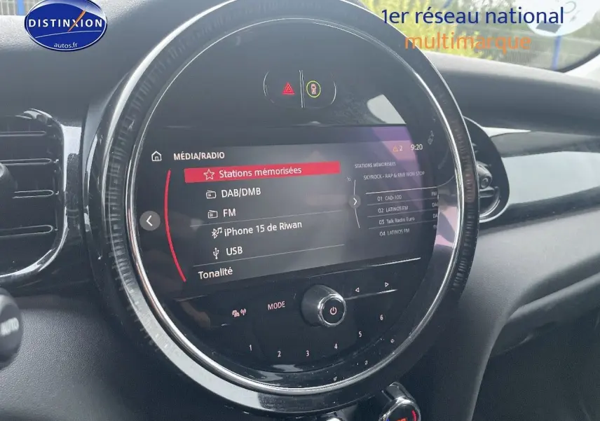 Gros plan sur l'écran central rond du tableau de bord d'une MINI blanche nacrée, affichant le menu média et radio.