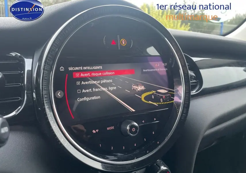 Vue rapprochée du tableau de bord de la MINI blanche nacrée 2023 montrant l'écran central avec alertes de sécurité active.