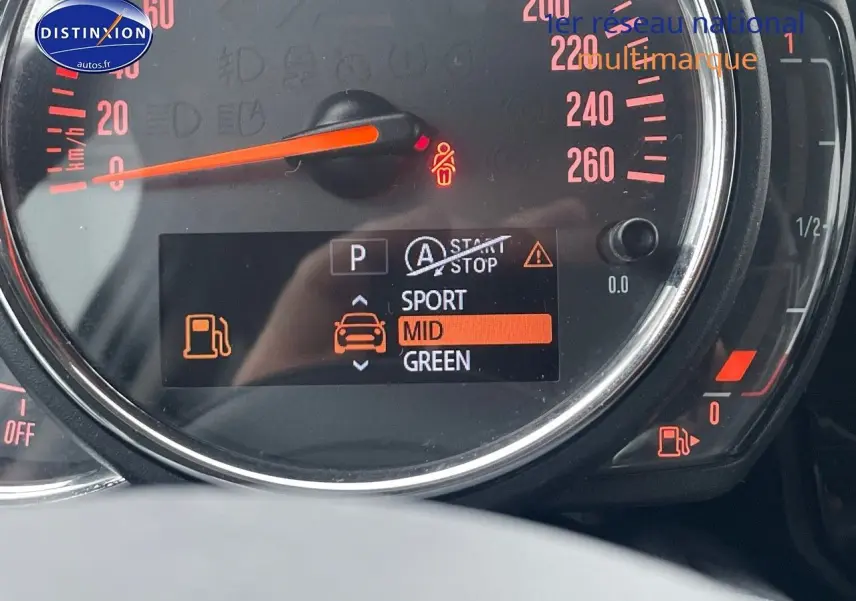 Gros plan sur le tableau de bord digital d'une MINI blanche nacrée 2023, affichant le mode de conduite et jauge d'essence.