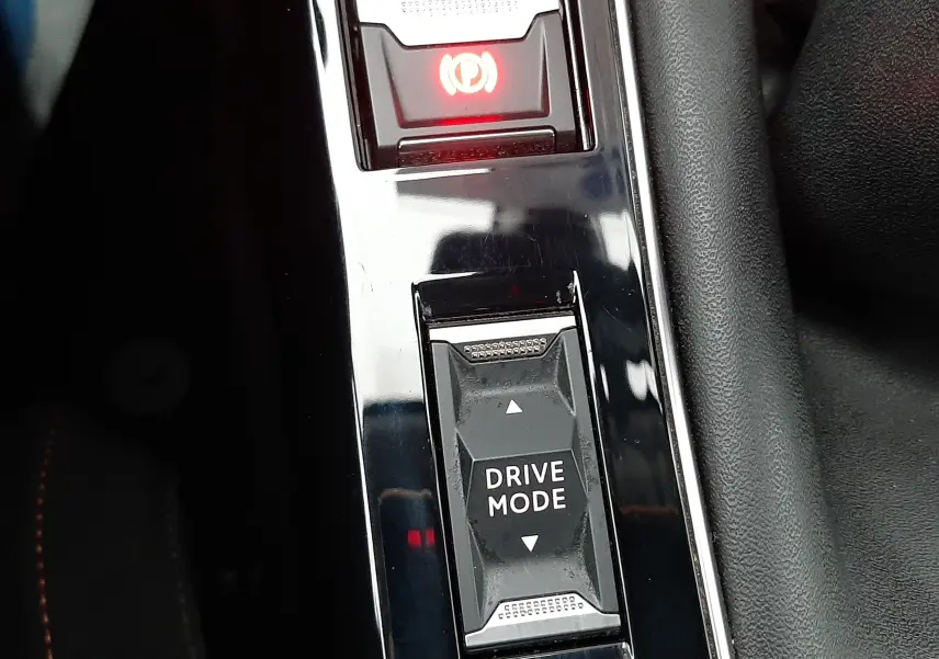 Gros plan sur la console centrale noire de la Peugeot 508 blanche, montrant le bouton Drive Mode et le frein à main électronique.