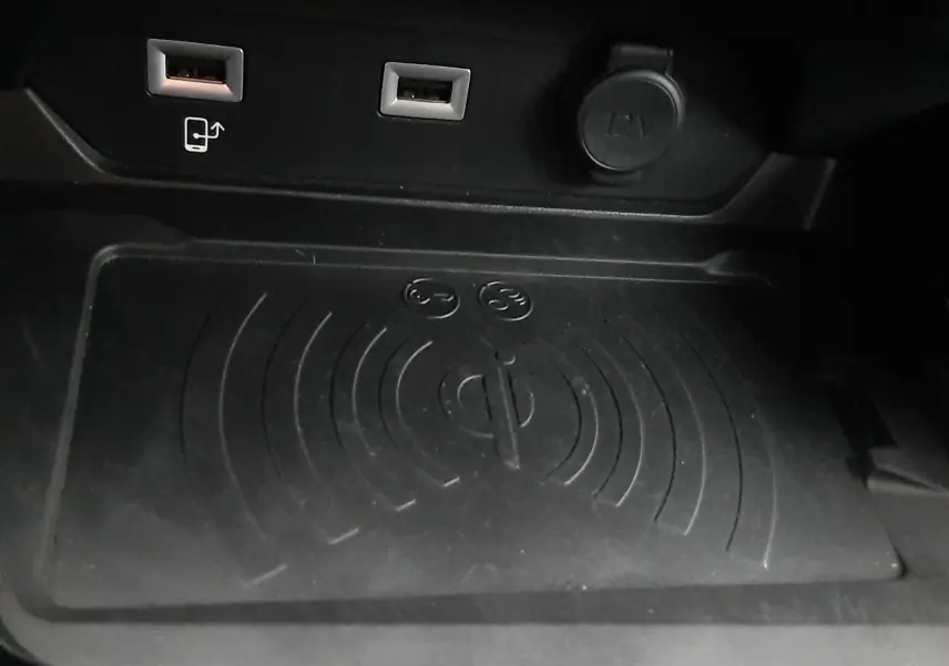Gros plan sur la console centrale noire de la Peugeot 508 blanche, montrant les ports USB, prise 12V et zone de recharge sans fil Qi.