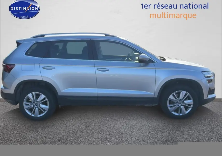 Vue latérale droite d'un Skoda Karoq gris 2025 avec barres de toit et jantes alliage.