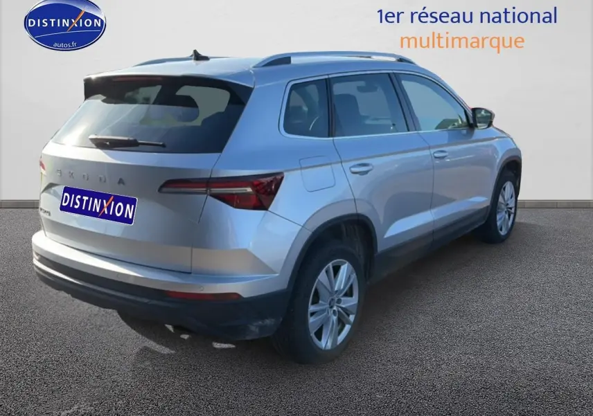 Vue 3/4 arrière droite d'un Skoda Karoq gris 2025 avec barres de toit et feux arrière LED visibles.