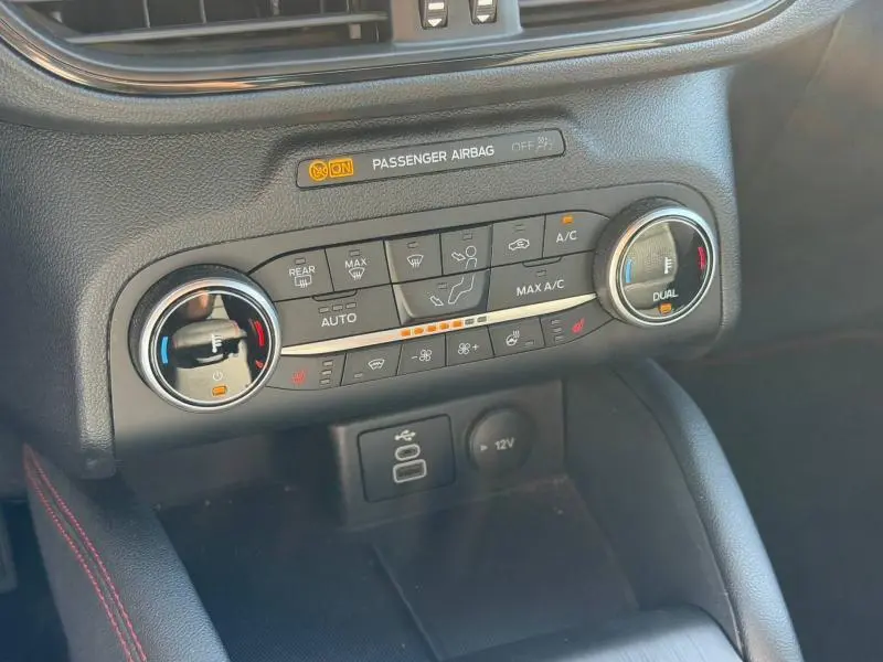 Gros plan sur la console centrale du Ford Kuga 2023, montrant les commandes de climatisation bi-zone et prises USB/12V.