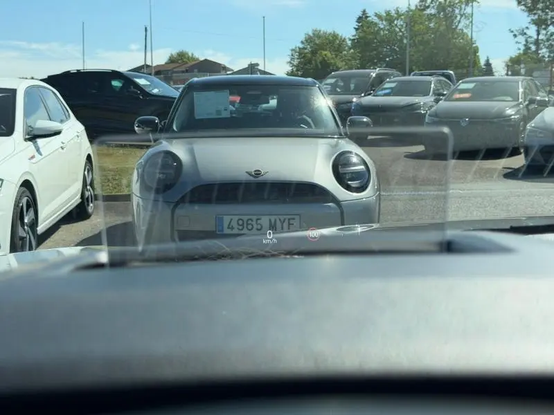 Vue avant d'une Mini grise stationnée, entourée de plusieurs autres véhicules sur un parking en plein jour.