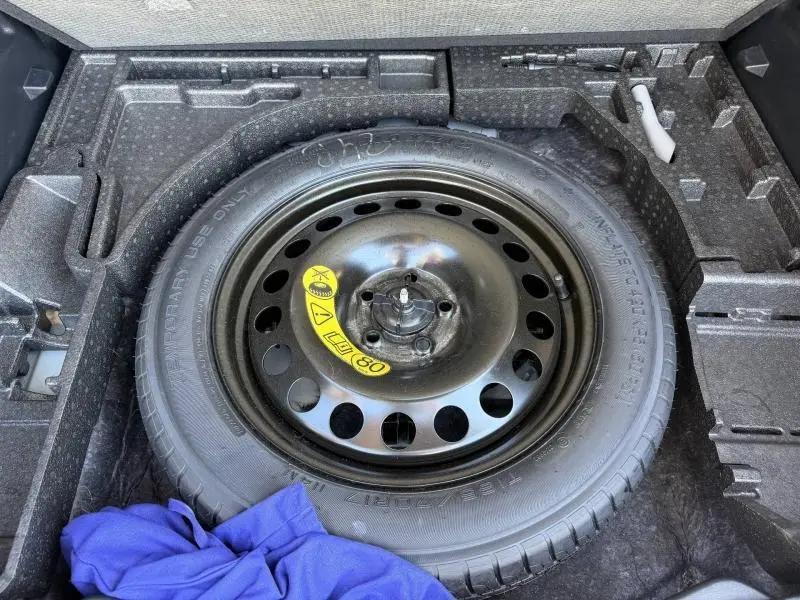 Vue en plongée sur la roue de secours noire dans le coffre d'un Ford Kuga gris Solar Métallisée 2023.
