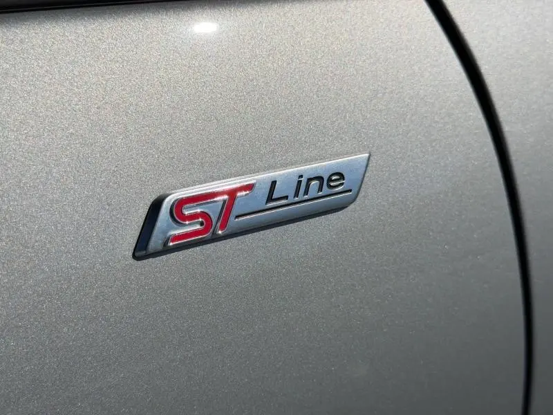 Gros plan sur l'écusson ST Line rouge et chrome sur la carrosserie gris Solar métallisée du Ford Kuga.
