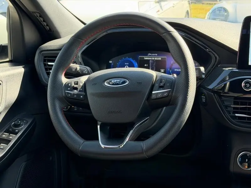 Vue rapprochée du volant cuir multifonction noir avec coutures rouges du Ford Kuga 2023, tableau de bord numérique en arrière-plan.