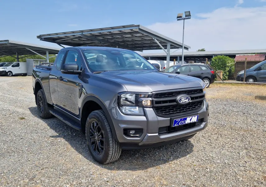 Ford Ranger Super Cabine gris carbone vu en 3/4 avant droit, avec barres de toit et marchepieds noirs visibles.