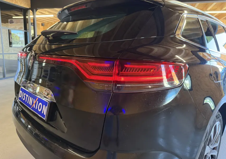 Vue 3/4 arrière droite d'une Renault Mégane Estate noire 2024 avec feux arrière allumés et toit ouvrant panoramique.
