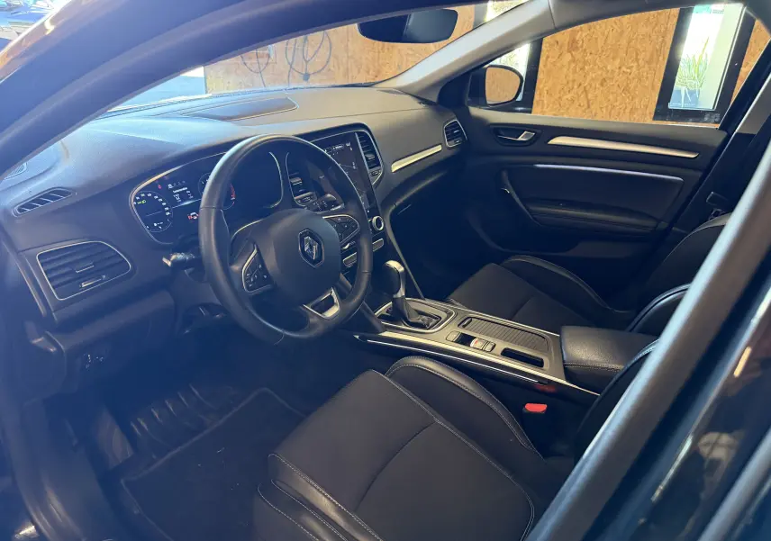 Vue intérieure côté conducteur de la Renault Mégane Estate noire 2024, avec tableau de bord et console centrale modernes.