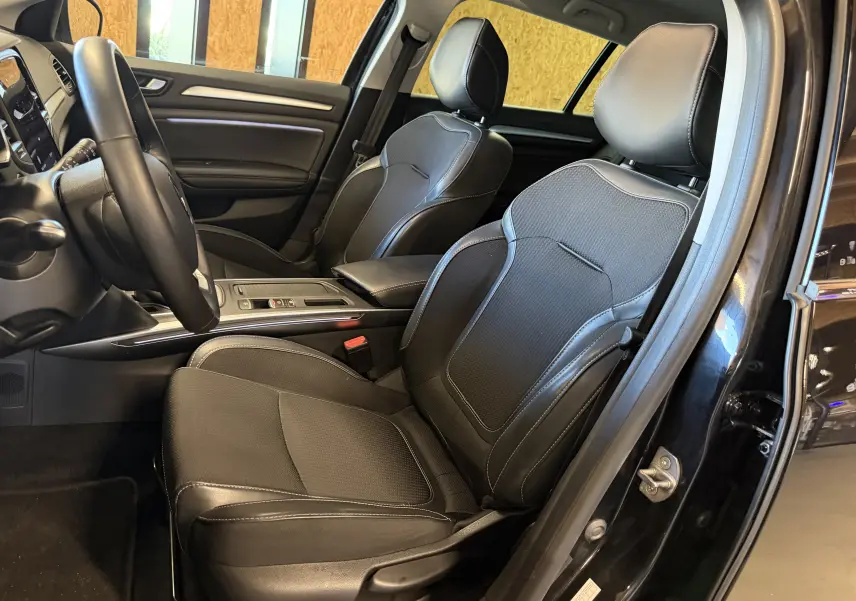 Intérieur avant droit de la Renault Mégane Estate 2024 noire, sièges en cuir noir avec surpiqûres blanches et console centrale moderne.