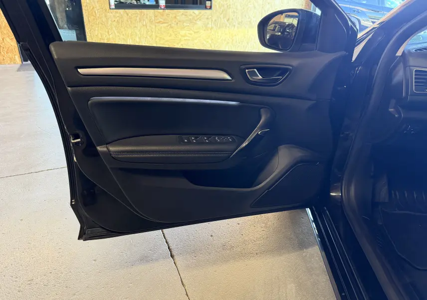 Vue intérieure de la porte avant gauche noire de la Renault Mégane Estate 2024 avec commandes de vitres et poignée argentée.