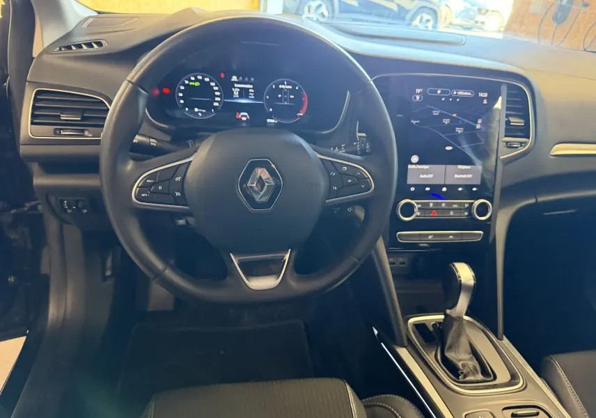 Vue intérieure de face du poste de conduite de la Renault Mégane Estate 2024 avec volant multifonction et écran tactile central.