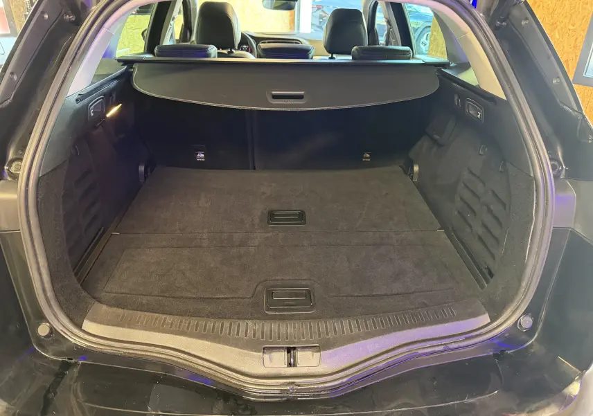 Coffre ouvert vu de l'arrière d'une Renault Mégane Estate noire 2024, avec cache-bagages et intérieur spacieux.