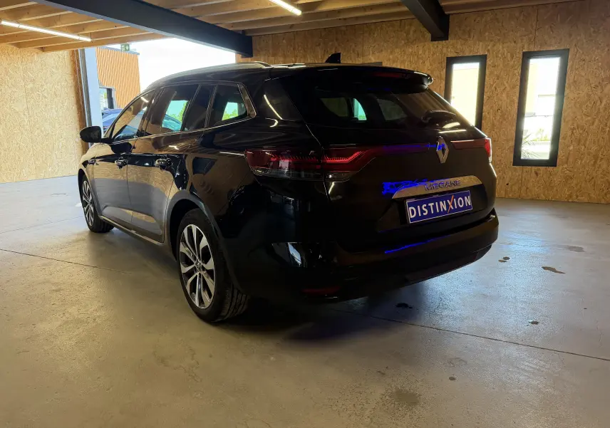 Renault Mégane Estate noir étoilé vue 3/4 arrière droit en intérieur avec feux arrière allumés.