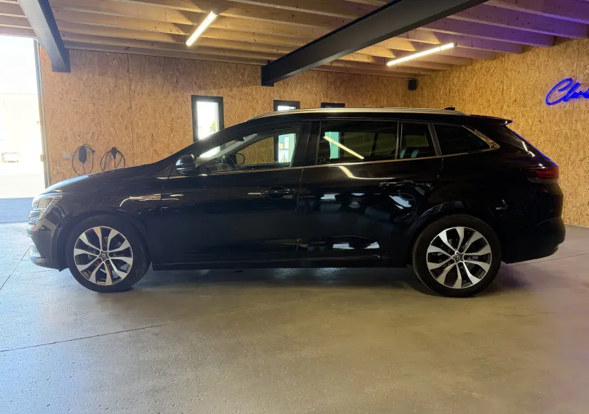 Renault Mégane Estate noir étoilé vue de profil côté gauche dans un garage avec toit en bois et éclairage intérieur.