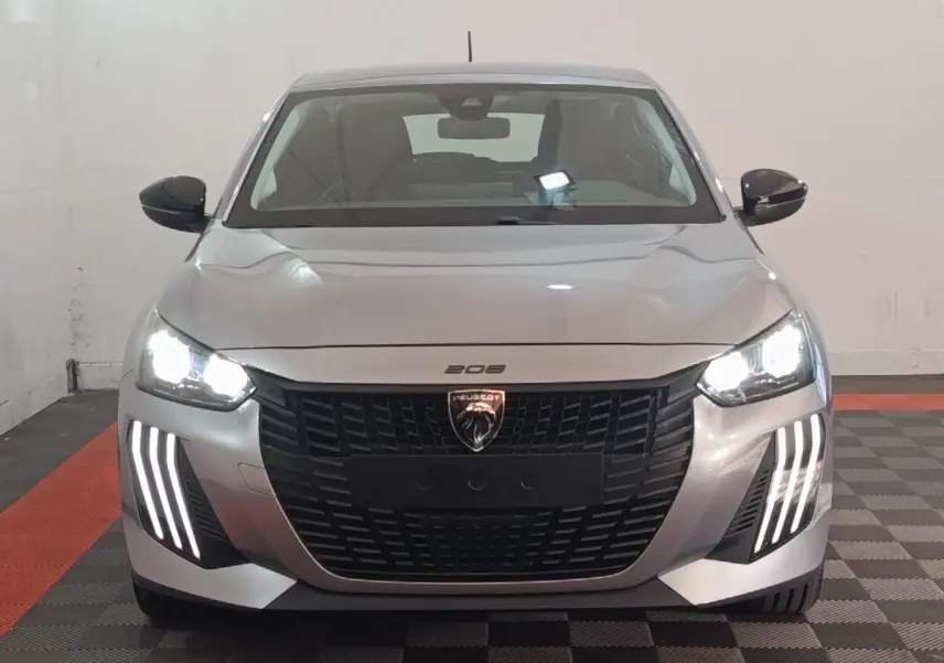 Peugeot 208 électrique gris clair vue de face avec phares LED allumés et signature lumineuse verticale distinctive.