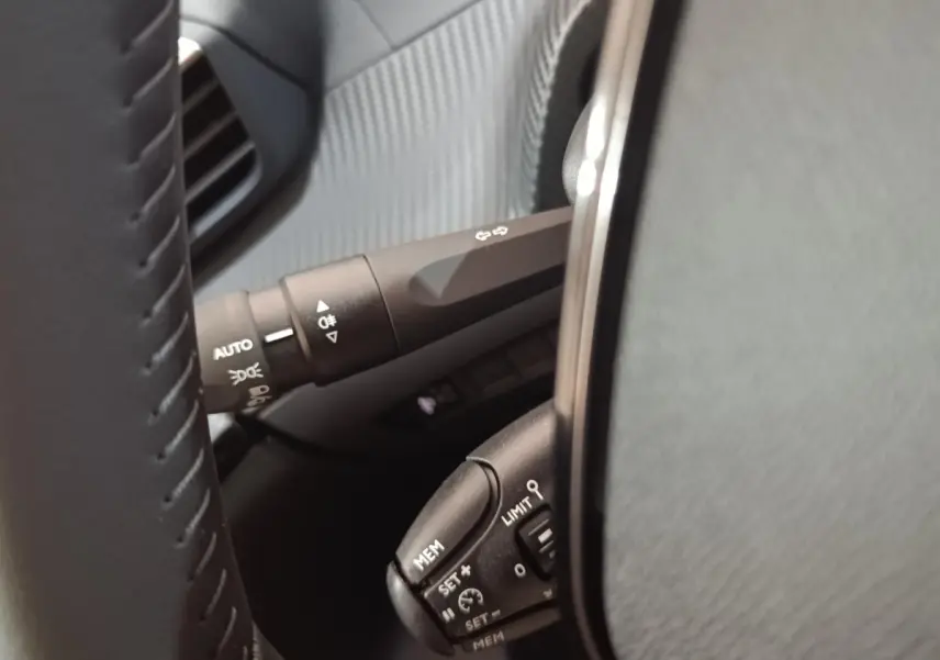 Gros plan sur le volant cuir noir de la Peugeot 208 électrique 2024, avec commandes de régulateur et éclairage.