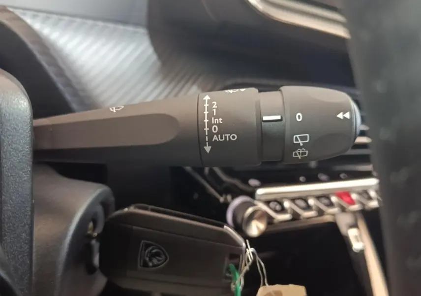 Gros plan sur la commande des essuie-glaces et clé insérée dans le contact d'un Peugeot 208 électrique gris clair, intérieur moderne.