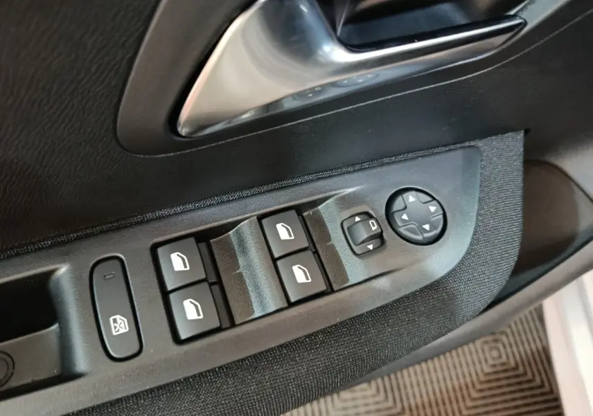 Gros plan sur les commandes de lève-vitres et rétroviseurs côté conducteur d’une Peugeot 208 électrique gris clair.