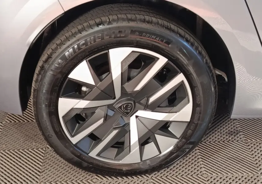 Gros plan sur la roue avant droite d'une Peugeot 208 électrique gris clair, avec jante au design géométrique moderne.
