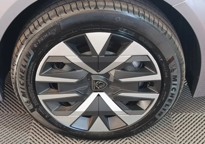 Gros plan sur la roue avant droite gris clair d'une Peugeot 208 électrique 2024 avec jante au design géométrique bicolore.