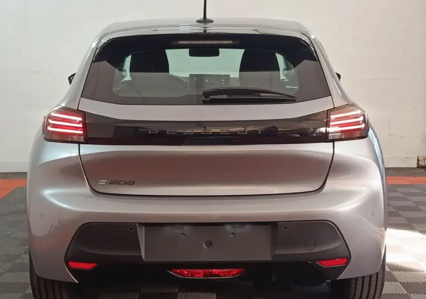 Vue arrière d'une Peugeot 208 électrique gris clair avec feux LED et logo PEUGEOT lumineux sur la malle.