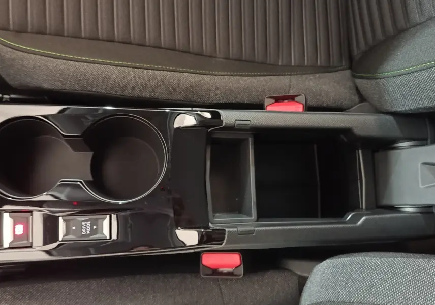 Vue plongeante sur la console centrale noire brillante de la Peugeot 208 électrique, avec porte-gobelets et rangement ouvert.