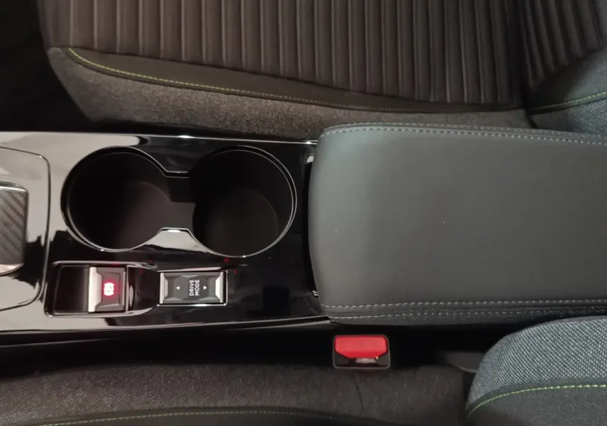 Vue intérieure rapprochée du tunnel central noir brillant avec accoudoir cuir et porte-gobelets de la Peugeot 208 électrique gris clair.