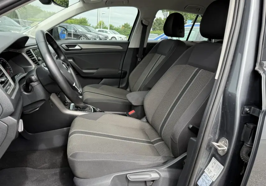 Vue intérieure côté conducteur du Volkswagen T-Roc gris Indium Metal, montrant les sièges avant et le volant multifonction en cuir.