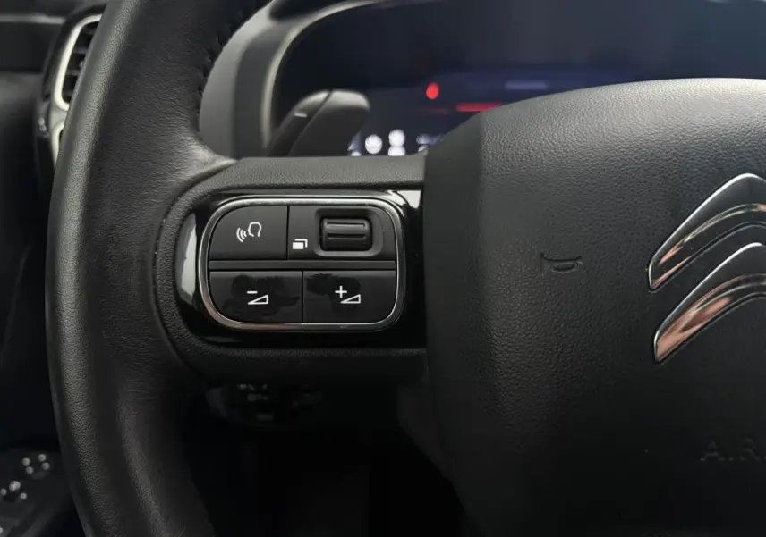 Gros plan sur le volant noir du Citroën C5 Aircross Hybrid 2024, avec commandes intégrées à gauche et logo chromé central.