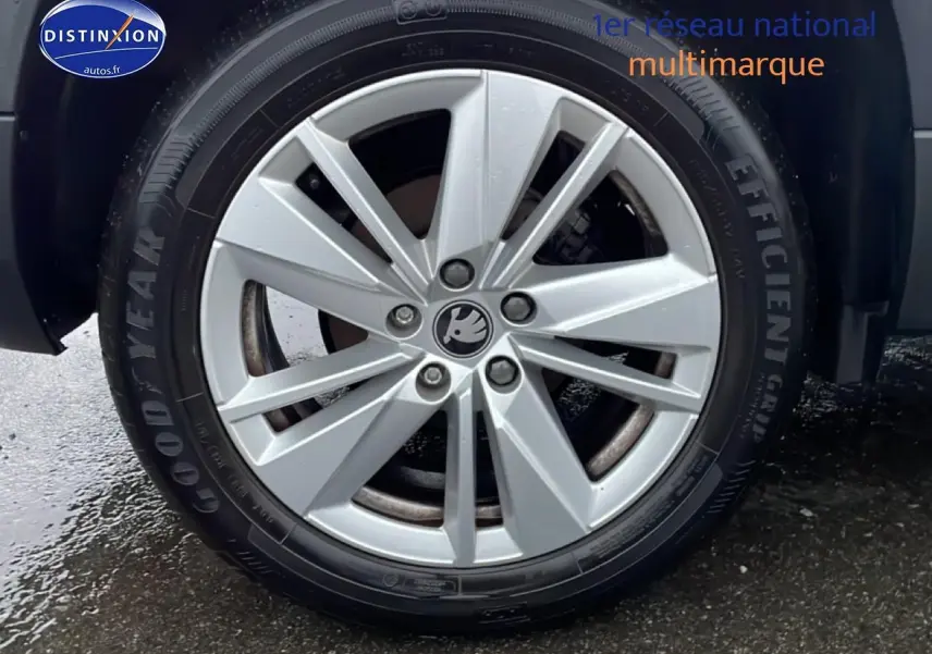 Gros plan sur la jante alu argentée d'une Skoda Karoq blanc glacial, pneu Goodyear visible sur sol humide.