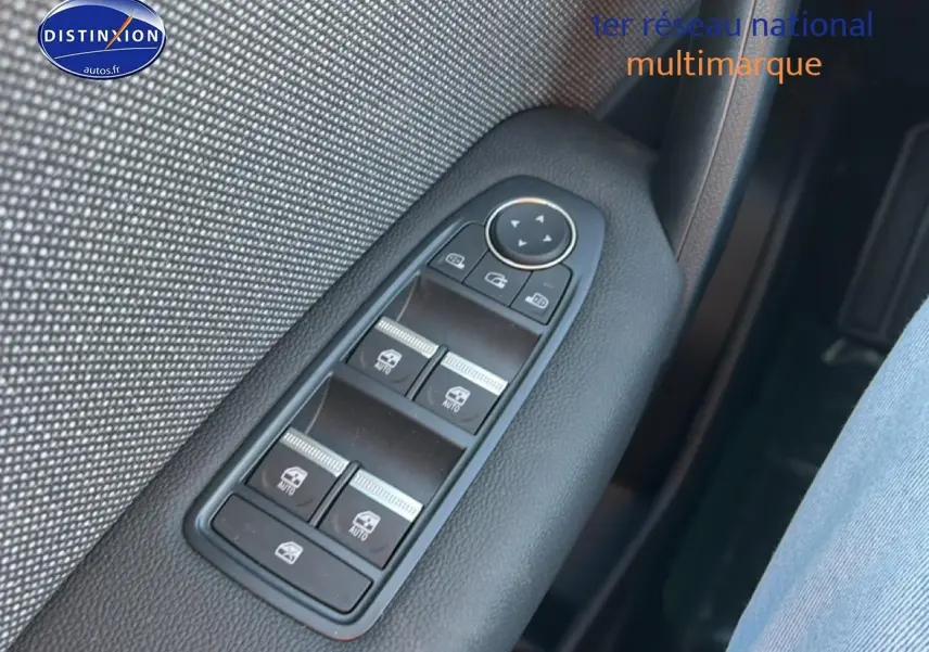 Gros plan sur les commandes des vitres électriques côté gauche, avec garniture textile grise et plastique noir.