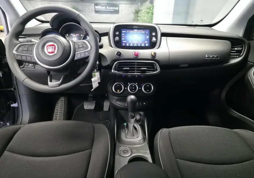 Vue intérieure avant du tableau de bord gris titane et volant noir du Fiat 500X 2024 avec écran tactile central et levier de boîte automatique.