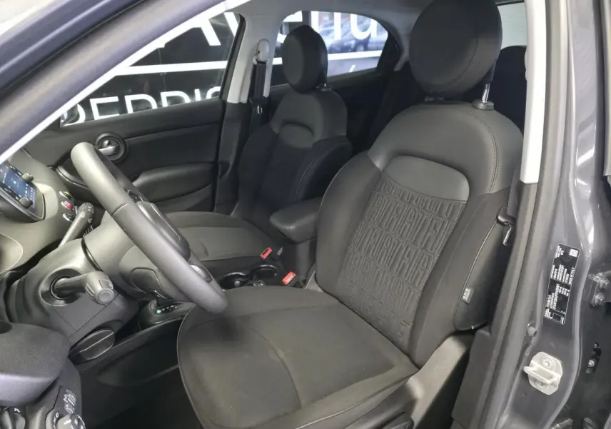 Vue intérieure côté conducteur du Fiat 500X gris, mettant en valeur les sièges en tissu noir avec monogramme Fiat.