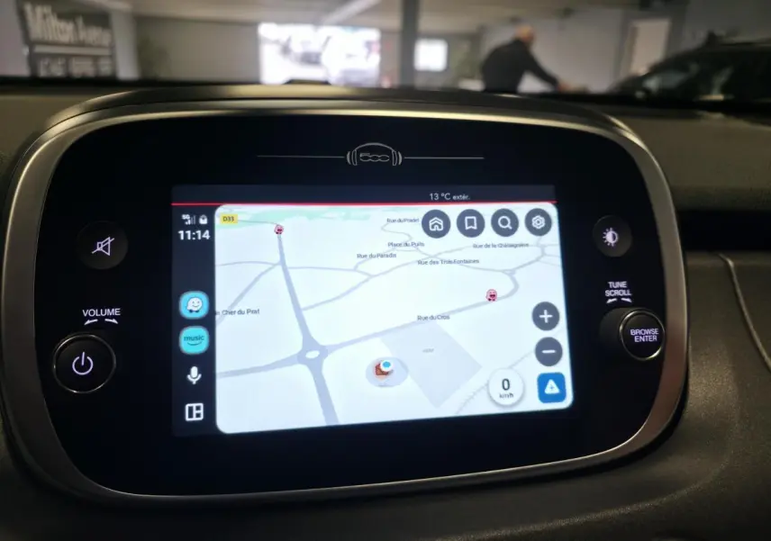 Écran tactile central avec navigation GPS allumée dans le tableau de bord d'une Fiat 500X gris 2024.