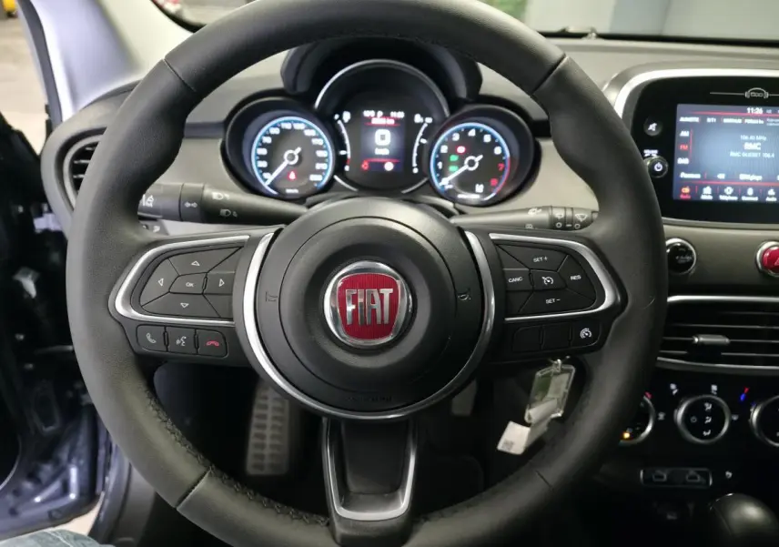 Vue rapprochée du volant noir de la Fiat 500X 2024 avec tableau de bord et écran tactile visible en arrière-plan.