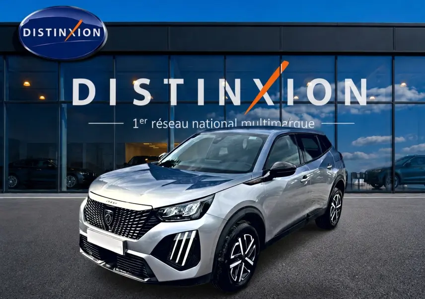 Peugeot 2008 gris en 3/4 avant droit, avec calandre noire et feux LED distinctifs, devant une vitrine Distinxion.
