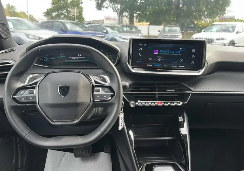 Vue intérieure avant centrée sur le volant et l'écran tactile du tableau de bord du Peugeot 2008 gris 2025.