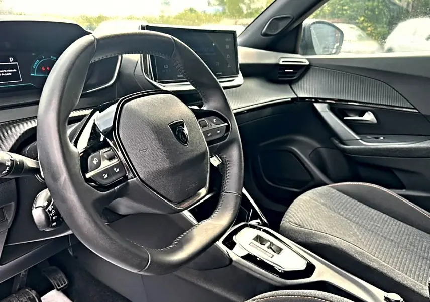 Intérieur de la Peugeot 2008 1.2 hybrid 145 style e-dcs6 2025, vue côté conducteur sur volant et console centrale noire.