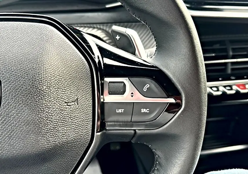 Gros plan sur le volant noir de la Peugeot 2008 1.2 hybrid 145 style, avec commandes multifonctions visibles.