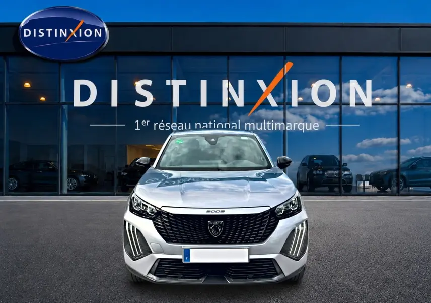 Vue frontale d'un Peugeot 2008 gris 2025 avec calandre noire et feux LED verticaux, devant une vitrine Distinxion.