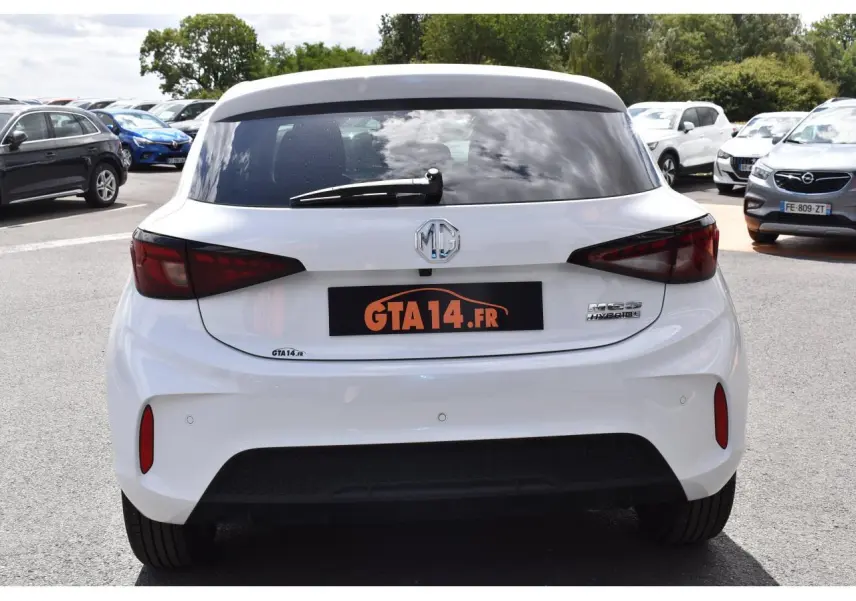 Vue arrière d'une MG3 blanche hybride 2026 avec feux arrière foncés et logo MG visible sur un parking.